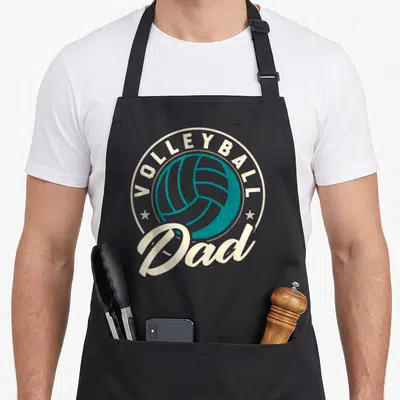 Beach sports dad apron - Teal volleyball inside cream circle with VOLLEYBALL Dad text and two stars — shown on a black cotton canvas apron against a white background