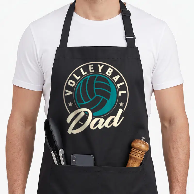 Beach sports dad apron - Teal volleyball inside cream circle with VOLLEYBALL Dad text and two stars — shown on a black cotton canvas apron against a white background