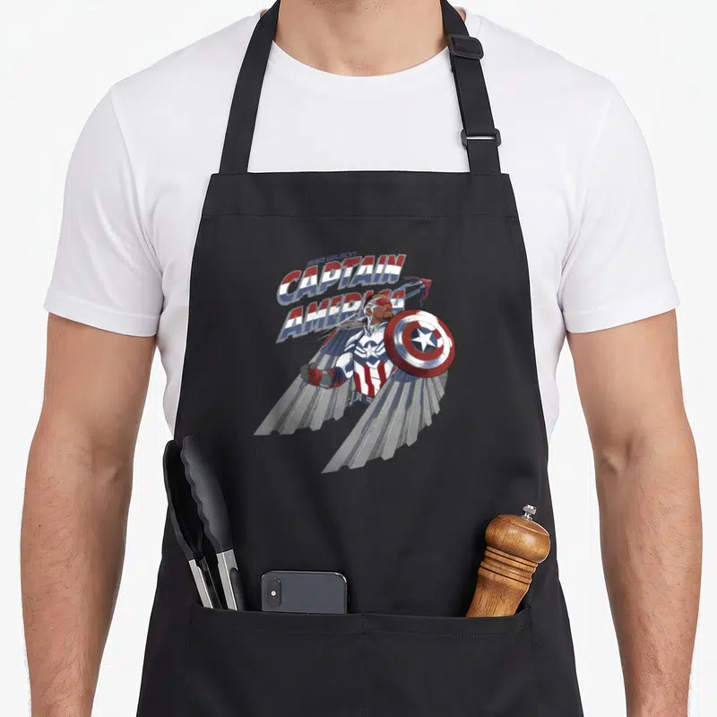 Sam falcon apron - Sam Wilson Captain America cartoon with spread wings and shield — shown on a black cotton canvas apron against a white background