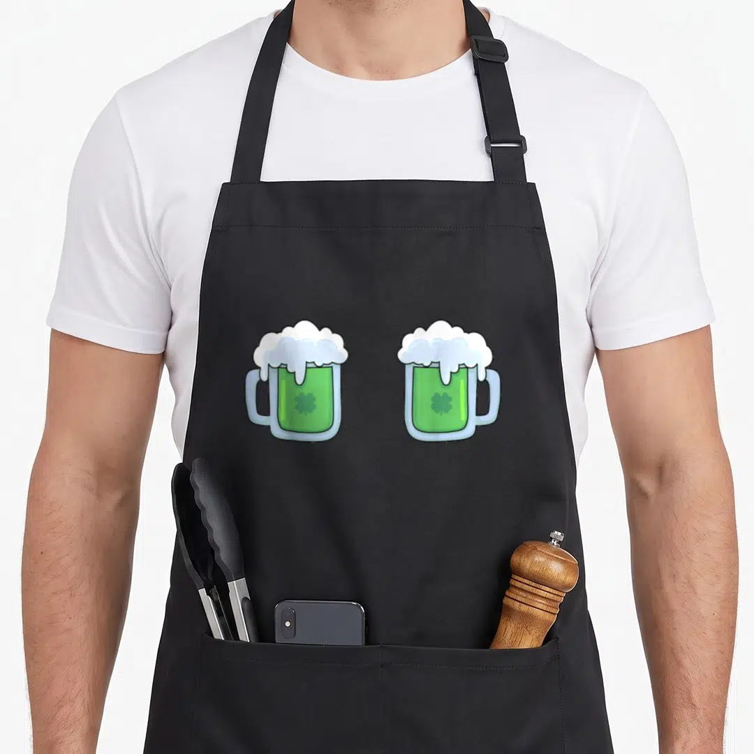Mug st patrick day aprons - Two cartoon green beer mugs with white foam and shamrocks side by side — shown on a black cotton canvas apron against a white background