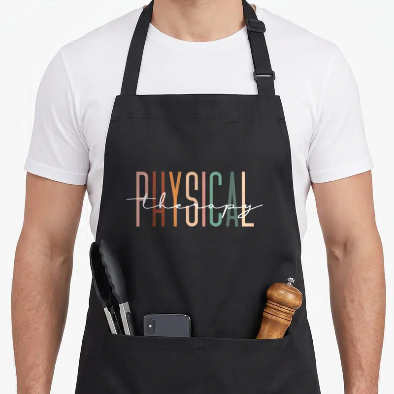 Student my therapy apron - Stacked PHYSICAL block letters in tan and green with white therapy script overlay — shown on a black cotton canvas apron against a white background
