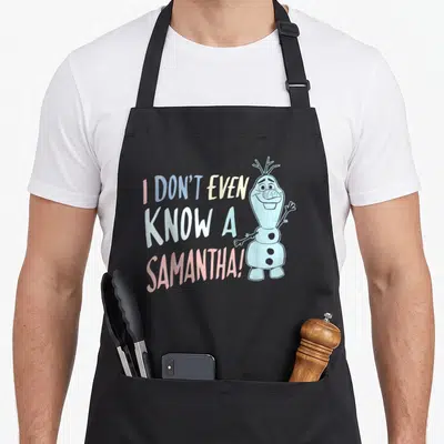 Even frozen apron - Stacked text I DON'T EVEN KNOW A SAMANTHA next to standing snowman in pastel colors — shown on a black cotton canvas apron against a white background