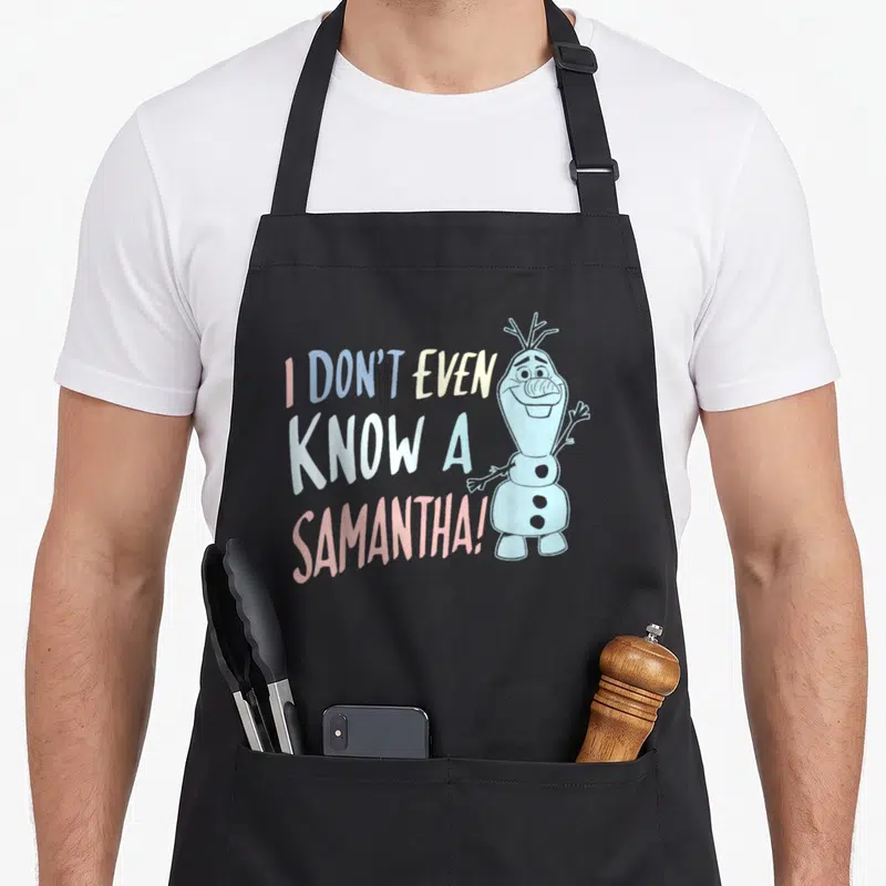 Even frozen apron - Stacked text I DON'T EVEN KNOW A SAMANTHA next to standing snowman in pastel colors — shown on a black cotton canvas apron against a white background
