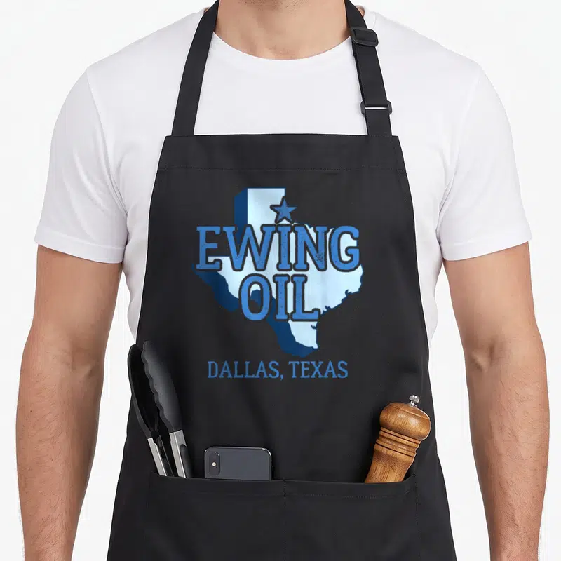 Ewing texas apron - Blue Texas map with Ewing Oil text and Dallas label — shown on a black cotton canvas apron against a white background