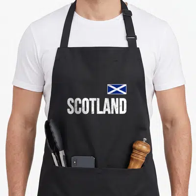 Flag scotland apron - Distressed white SCOTLAND text above a blue and white saltire flag — shown on a black cotton canvas apron against a white background