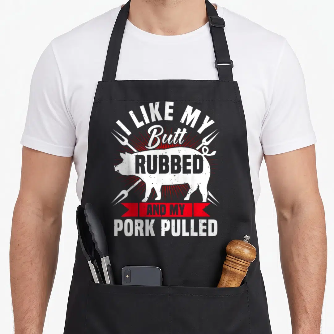 Pork pulled lover apron - Pig silhouette with I Like My Butt Rubbed And My Pork Pulled text — shown on a black cotton canvas apron against a white background