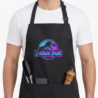 Gradient science apron - Dinosaur skeleton profile inside circle with blue purple gradient JURASSIC PARK banner — shown on a black cotton canvas apron against a white background