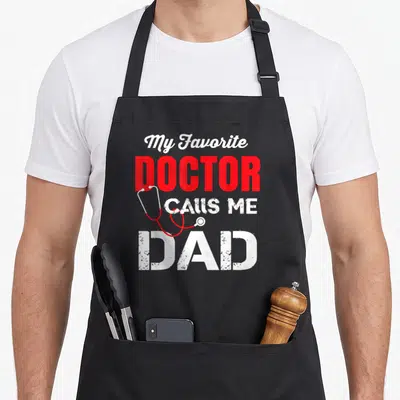 Vintage call doctor with apron - Red and white text My Favorite Doctor Calls Me Dad with draped stethoscope — shown on a black cotton canvas apron against a white background