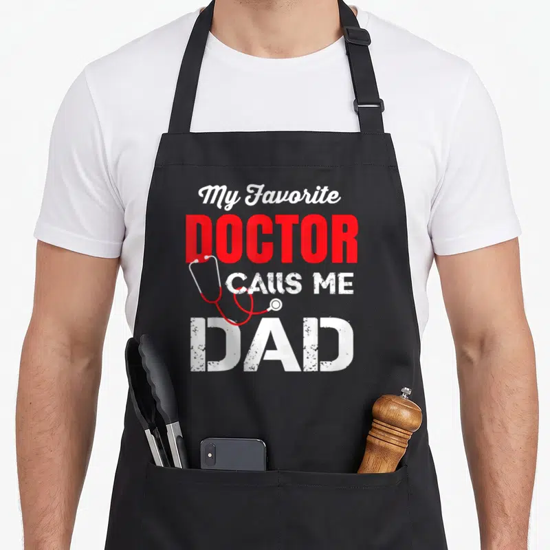 Vintage call doctor with apron - Red and white text My Favorite Doctor Calls Me Dad with draped stethoscope — shown on a black cotton canvas apron against a white background