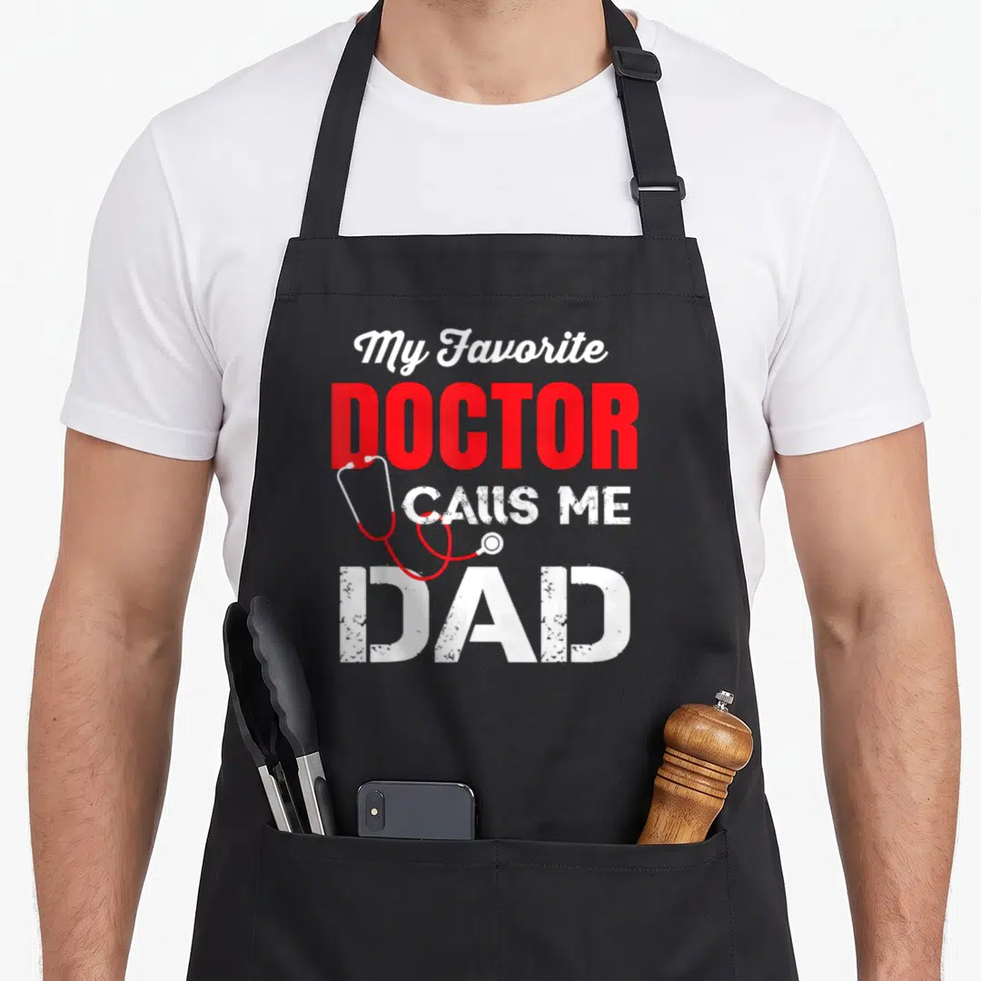 Vintage call doctor with apron - Red and white text My Favorite Doctor Calls Me Dad with draped stethoscope — shown on a black cotton canvas apron against a white background