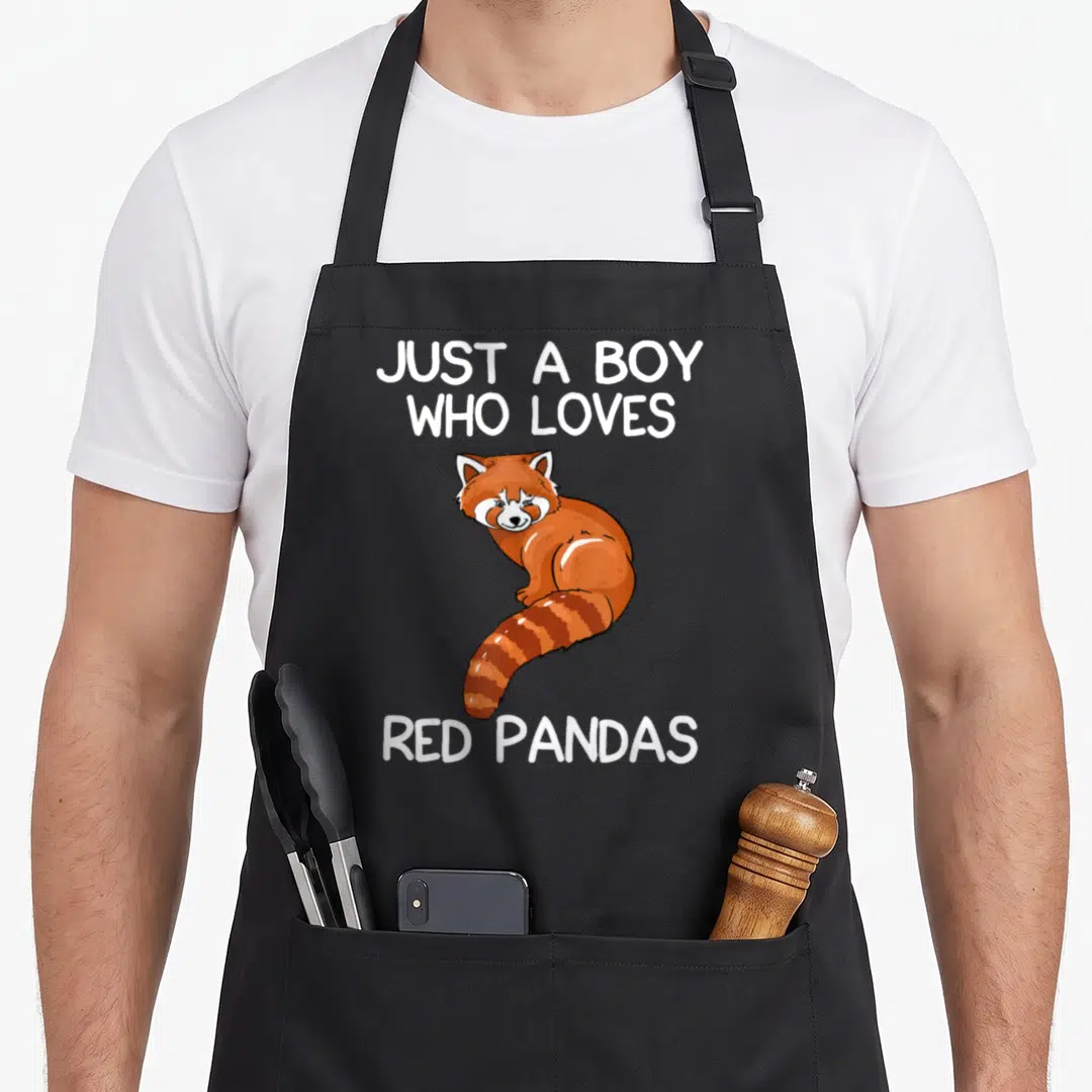 Vintage pandas panda apron - Cartoon red panda in orange and brown sandwiched between white text reading JUST A BOY WHO — shown on a black cotton canvas apron against a white background