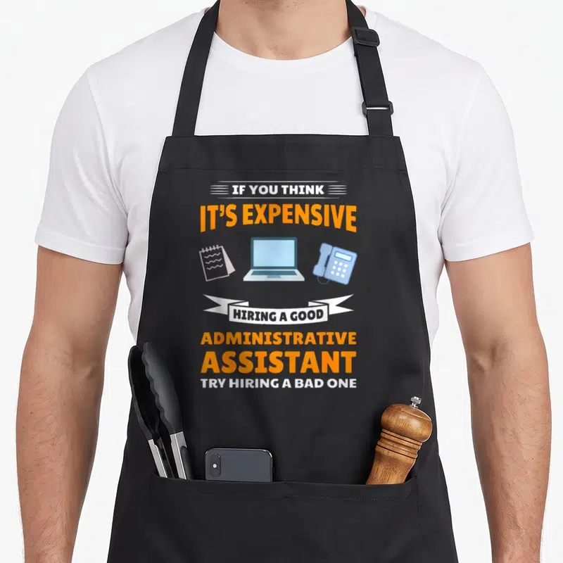Funny assistant administrative apron - Stacked orange and white text about hiring assistants above a laptop, phone — shown on a black cotton canvas apron against a white background