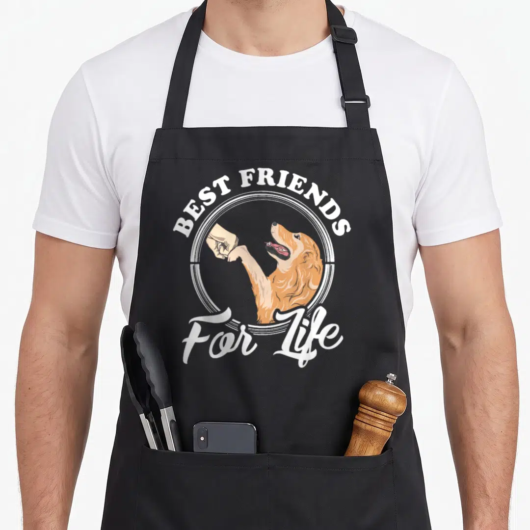 Funny golden retriever apron - Cartoon orange dog and human hand fist bumping inside white circle with best friends — shown on a black cotton canvas apron against a white background