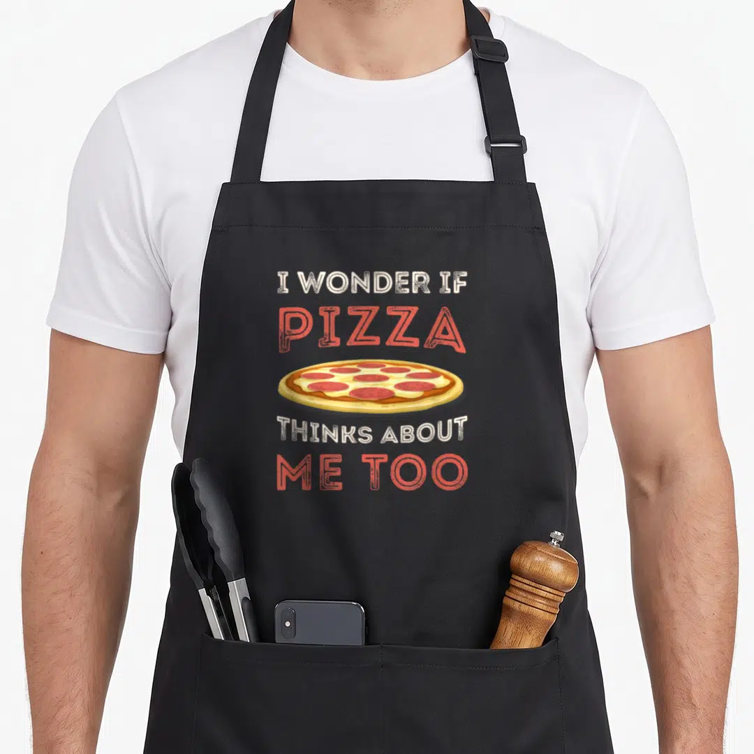 Dough pizza apron - I WONDER IF PIZZA THINKS ABOUT ME TOO text around a cartoon pepperoni slice — shown on a black cotton canvas apron against a white background