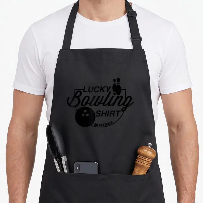 Wash bowling apron - Black shield design with Lucky Bowling Shirt text, ball, and two pins — shown on a black cotton canvas apron against a white background
