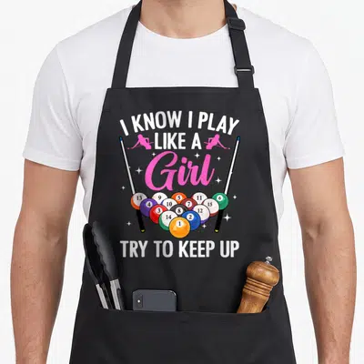 Funny pool billiards apron - I KNOW I PLAY LIKE A Girl text with two pink silhouettes, 15 numbered balls, and two pool — shown on a black cotton canvas apron against a white background