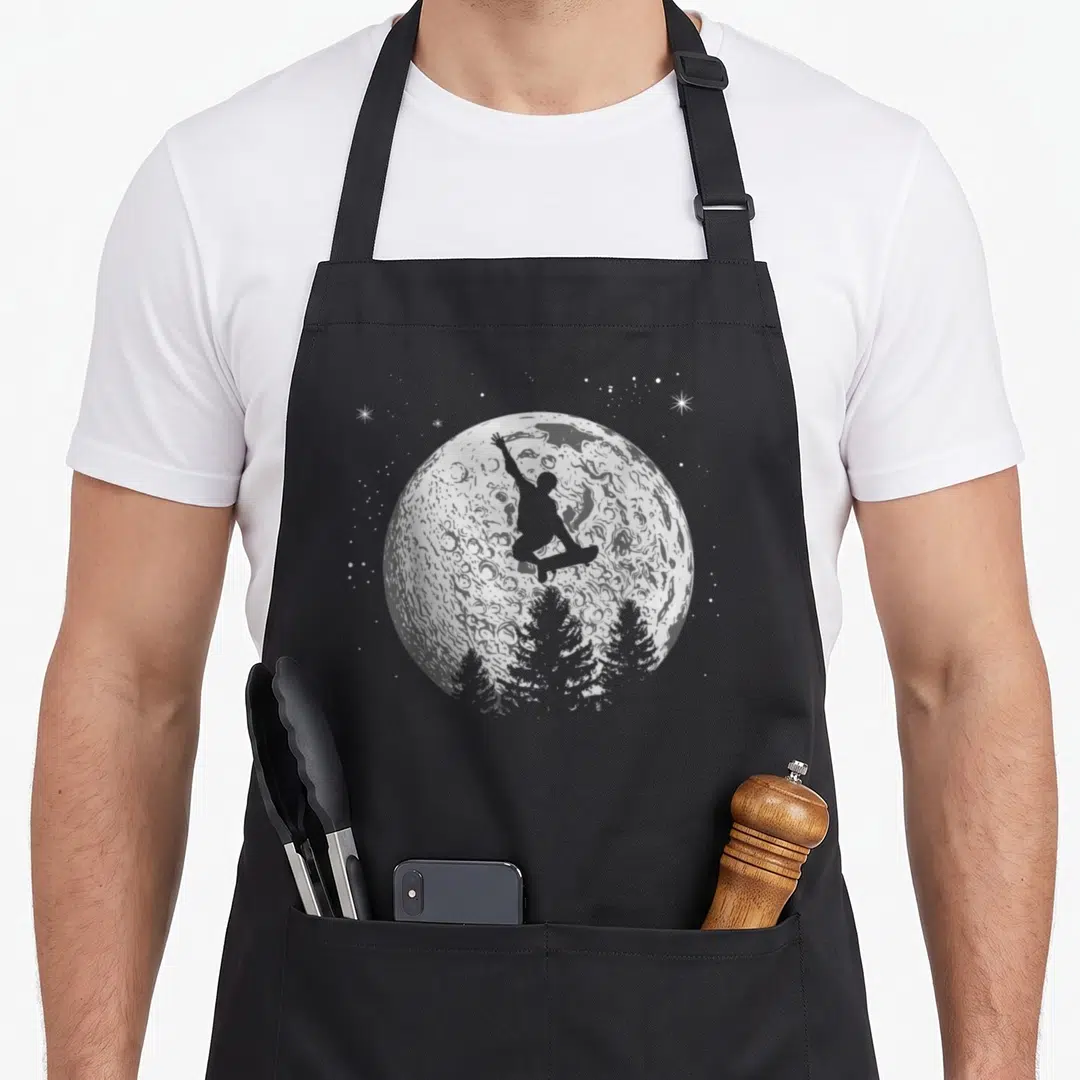 Stunt skateboard funny apron - Grey moon with jumping snowboarder silhouette, pine trees, and white stars — shown on a black cotton canvas apron against a white background