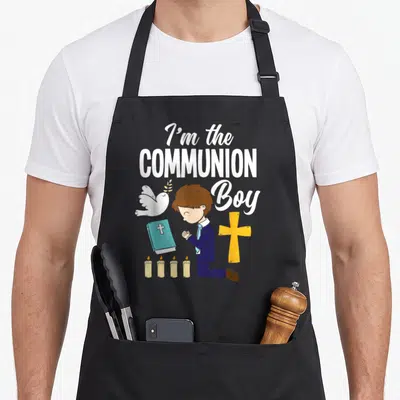 1st communion aprons - Cartoon boy kneeling with dove, cross, bible, four candles, and 'I'm the COMMUNION Boy' text — shown on a black cotton canvas apron against a white background