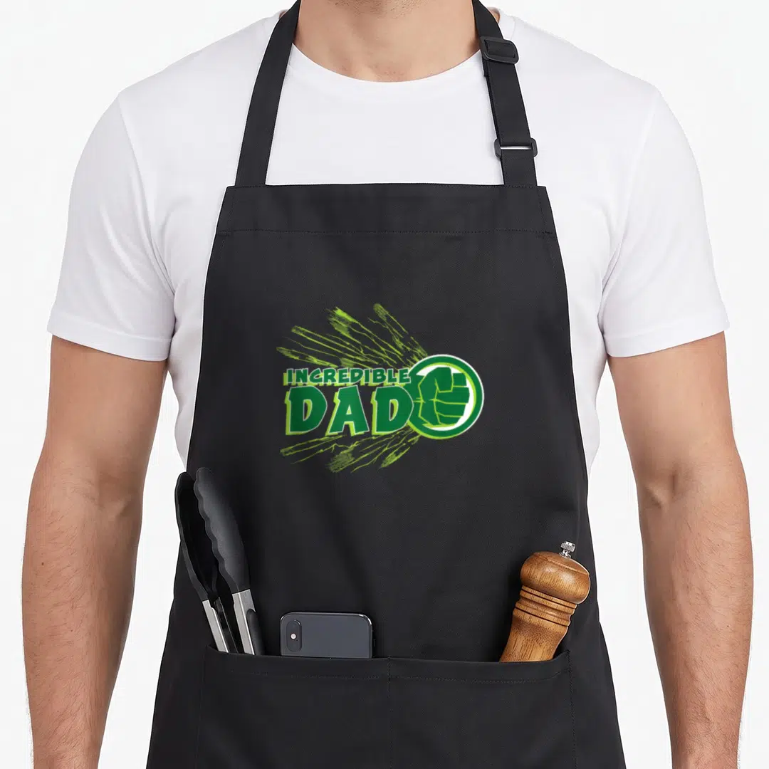Vacation father day apron - Incredible Dad text with green fist in white circle and energy lines — shown on a black cotton canvas apron against a white background