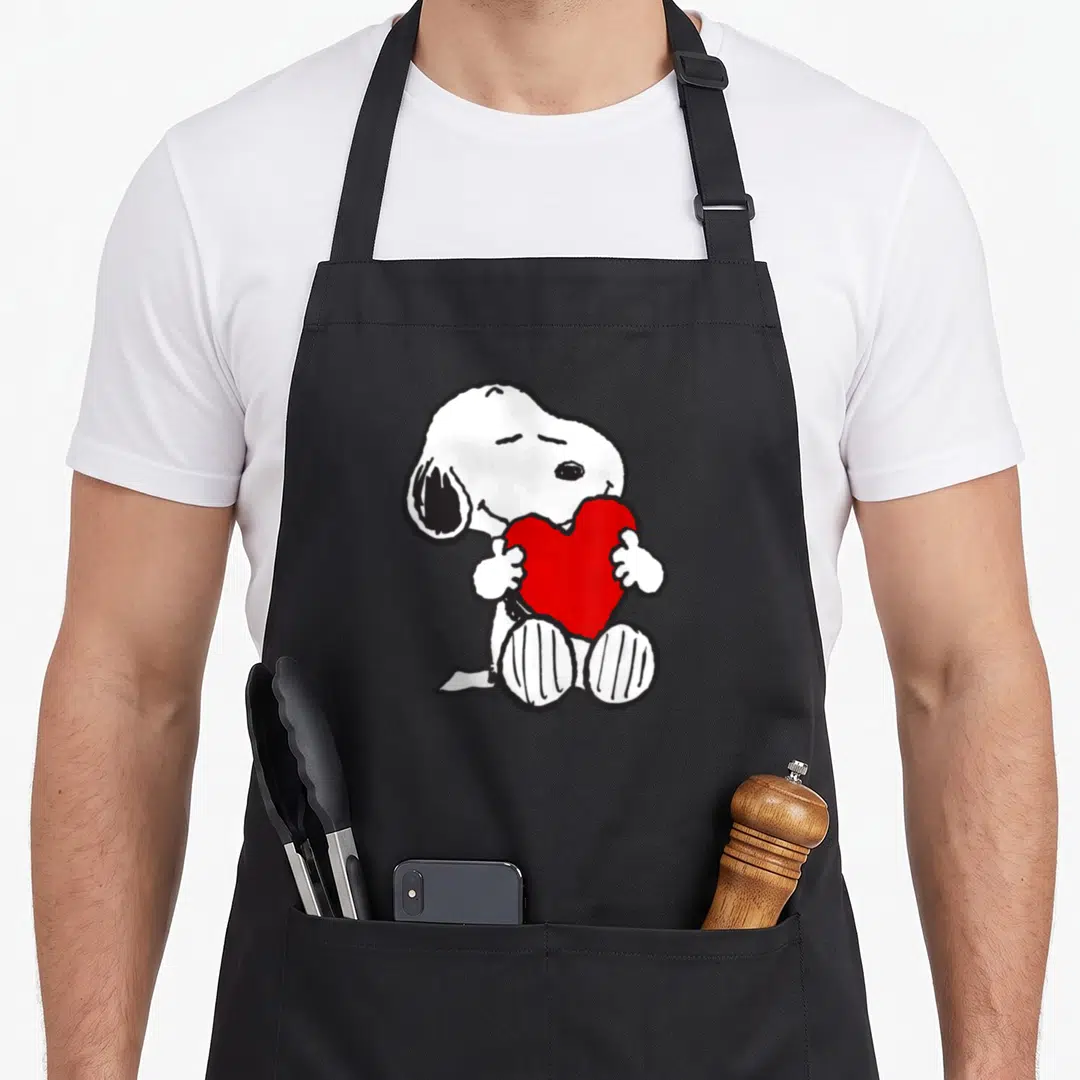 Hugging valentine apron - White cartoon dog sitting and hugging a large red heart outlined in black on a dark background — shown on a black cotton canvas apron against a white background