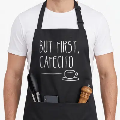 Cafe coffee apron - White stacked text but first cafecito above horizontal line and cup on saucer — shown on a black cotton canvas apron against a white background