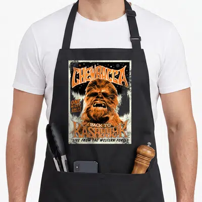 Kashyyyk concert apron - Retro orange and black poster art of Chewbacca with arched text reading Back to Kashyyyk — shown on a black cotton canvas apron against a white background
