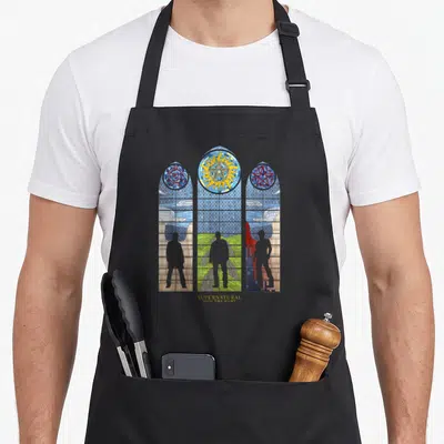 Funny glass stained apron - Three panel stained glass window with symbols, grey silhouettes, and text SUPERNATURAL JOIN — shown on a black cotton canvas apron against a white background