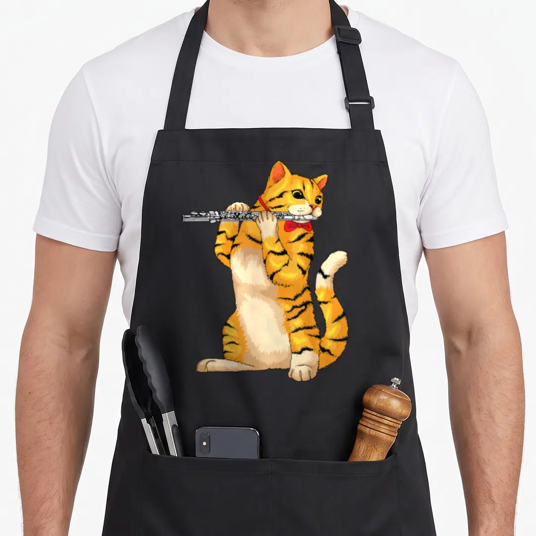 Fluter cat apron - Orange tabby cat sitting and playing a silver flute with a red bow tie — shown on a black cotton canvas apron against a white background