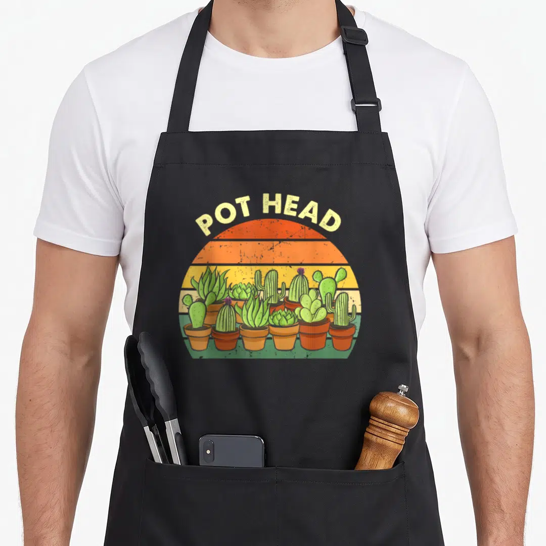 Pot gardener apron - POT HEAD text over retro striped sun with row of green cacti in terracotta pots — shown on a black cotton canvas apron against a white background