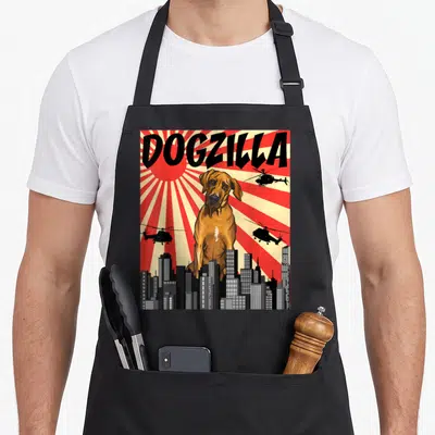 Japanese rhodesian ridgeback apron - Retro graphic of giant brown dog DOGZILLA looming over city with flying — shown on a black cotton canvas apron against a white background