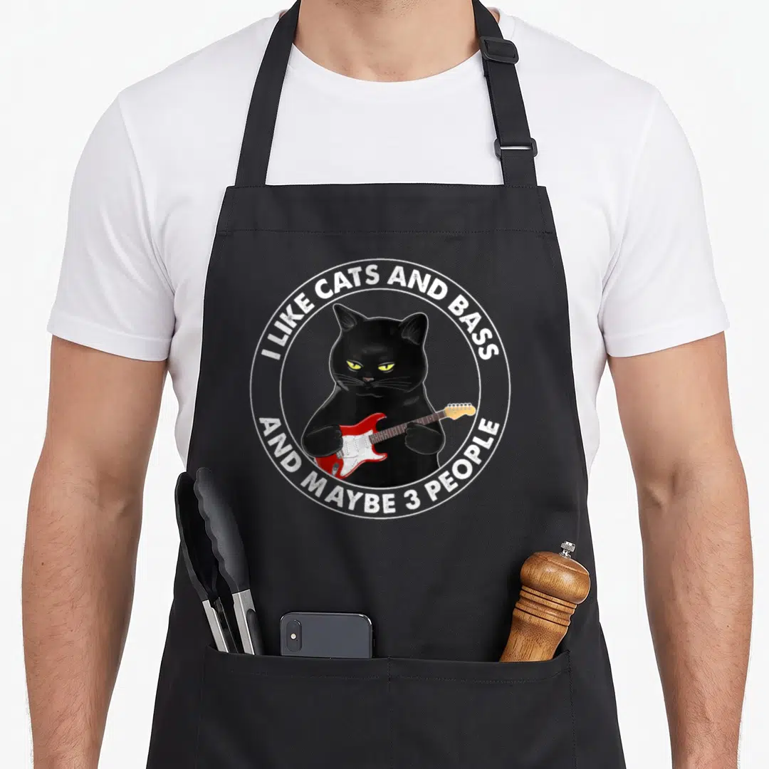 Bass maybe cat apron - Cartoon black cat holding red bass guitar inside white circle with text — shown on a black cotton canvas apron against a white background