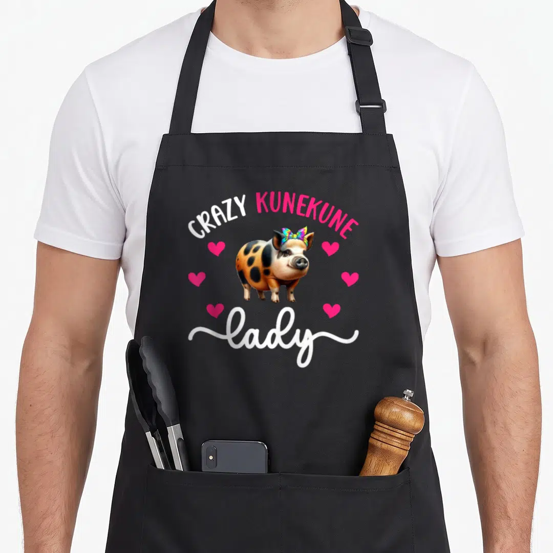 Kunekune crazy pig lady apron - Cartoon spotted pig with bow, CRAZY KUNEKUNE lady text, and six pink hearts — shown on a black cotton canvas apron against a white background