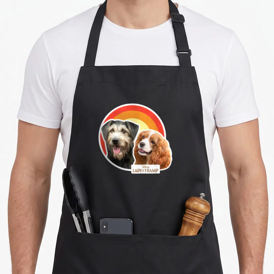 Live lady and the tramp apron - Two dogs beside red orange yellow rainbow with Disney text box — shown on a black cotton canvas apron against a white background