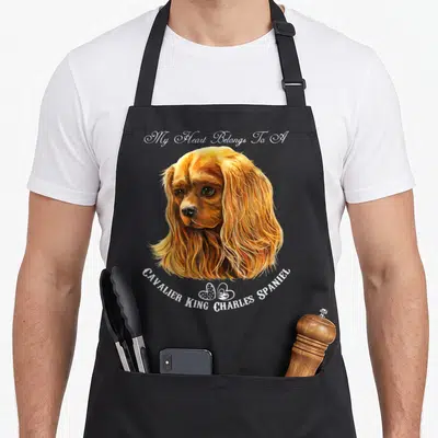 Ruby king apron - Realistic Cavalier King Charles Spaniel head in golden brown and white with arched text and two small — shown on a black cotton canvas apron against a white background
