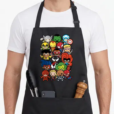 Heroe villain kawaii apron - Chibi superhero cluster in vertical oval with red blue yellow green black cartoon figures — shown on a black cotton canvas apron against a white background