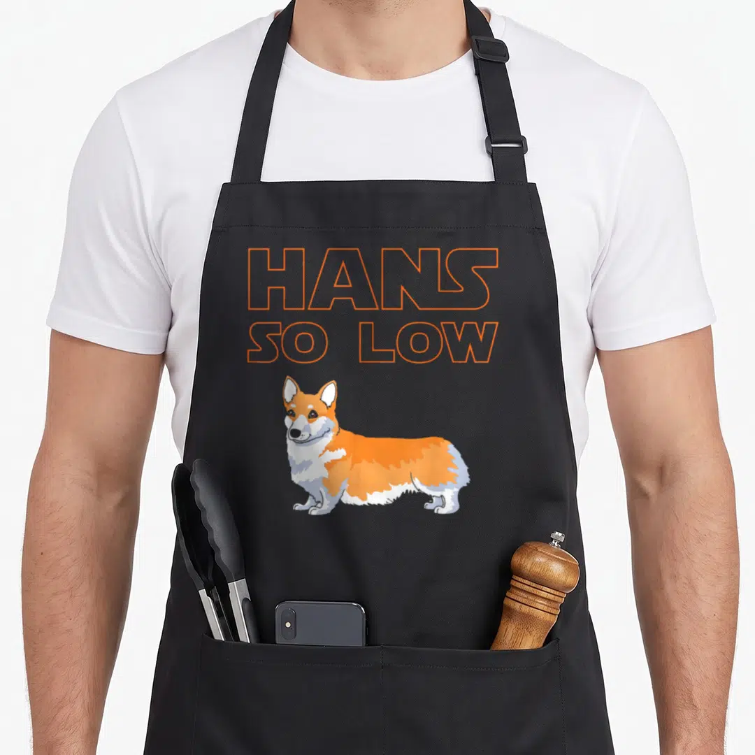 Han corgi apron - Orange outline HANS SO LOW text above standing cartoon corgi — shown on a black cotton canvas apron against a white background