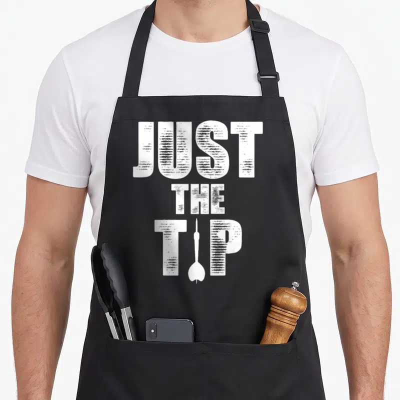 Tip shooting apron - White distressed text JUST THE TIP with single dart silhouette replacing the letter I in TIP — shown on a black cotton canvas apron against a white background