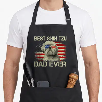 Shih dog dad apron - Shih Tzu in flag sunglasses with BEST SHIH TZU DAD EVER text on distressed background — shown on a black cotton canvas apron against a white background