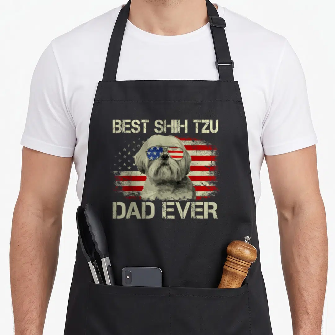 Shih dog dad apron - Shih Tzu in flag sunglasses with BEST SHIH TZU DAD EVER text on distressed background — shown on a black cotton canvas apron against a white background