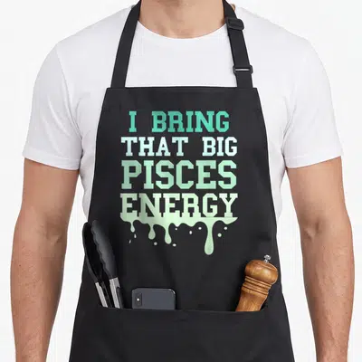 Pisce energy birthday apron - Stacked teal and green text reading I BRING THAT BIG PISCES ENERGY with dripping paint — shown on a black cotton canvas apron against a white background