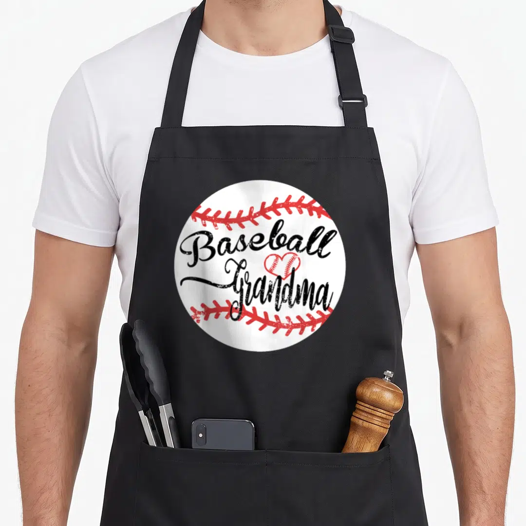 Proud baseball grandma apron - White circular baseball with red stitching and black Baseball Grandma text separated — shown on a black cotton canvas apron against a white background