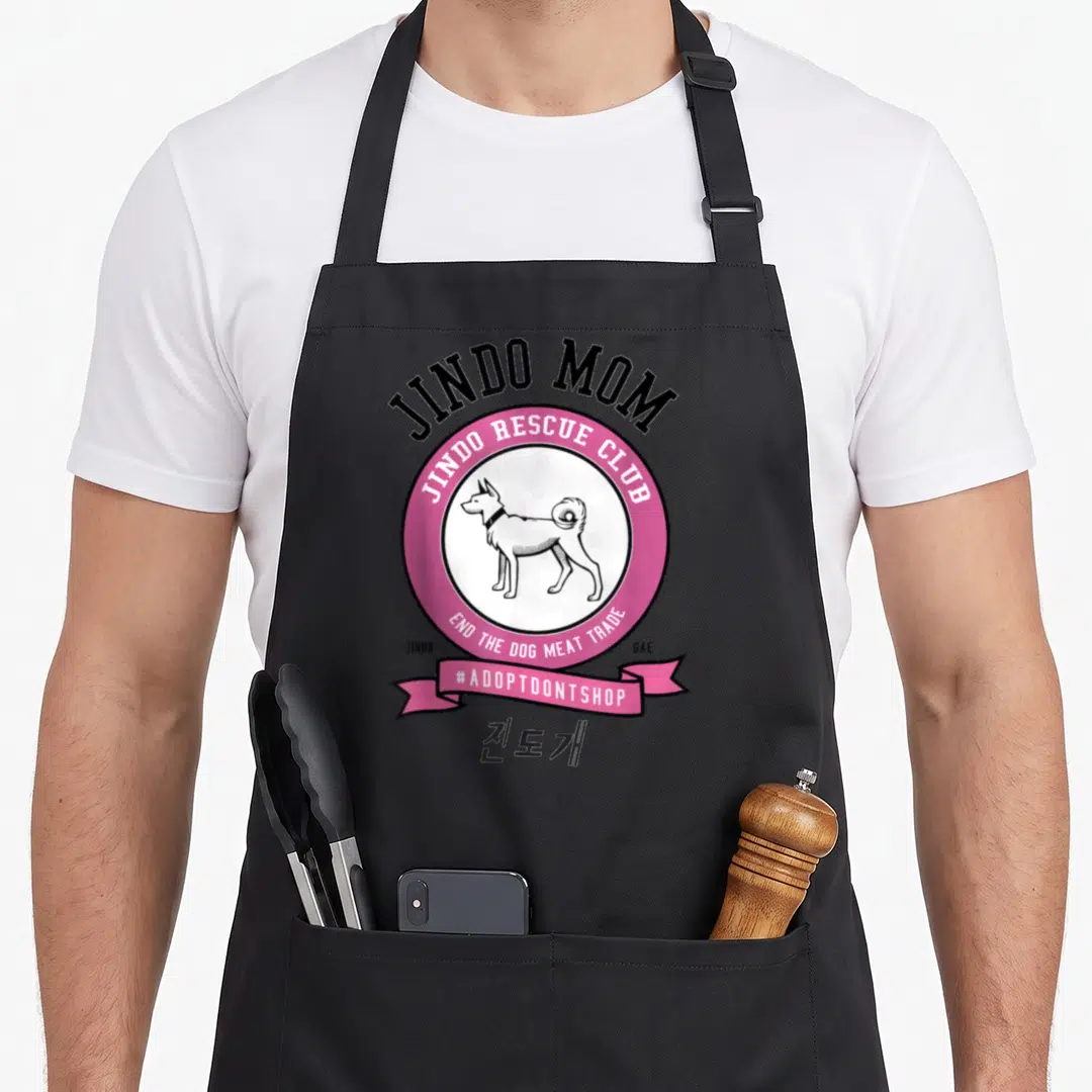 Jindo dog breed aprons - Pink circle with cartoon Jindo dog, rescue club text, and Korean characters below ribbon — shown on a black cotton canvas apron against a white background