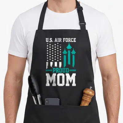 Usaf american flag apron - U.S. AIR FORCE PROUD MOM text with white stars and teal jet silhouettes in distressed style — shown on a black cotton canvas apron against a white background