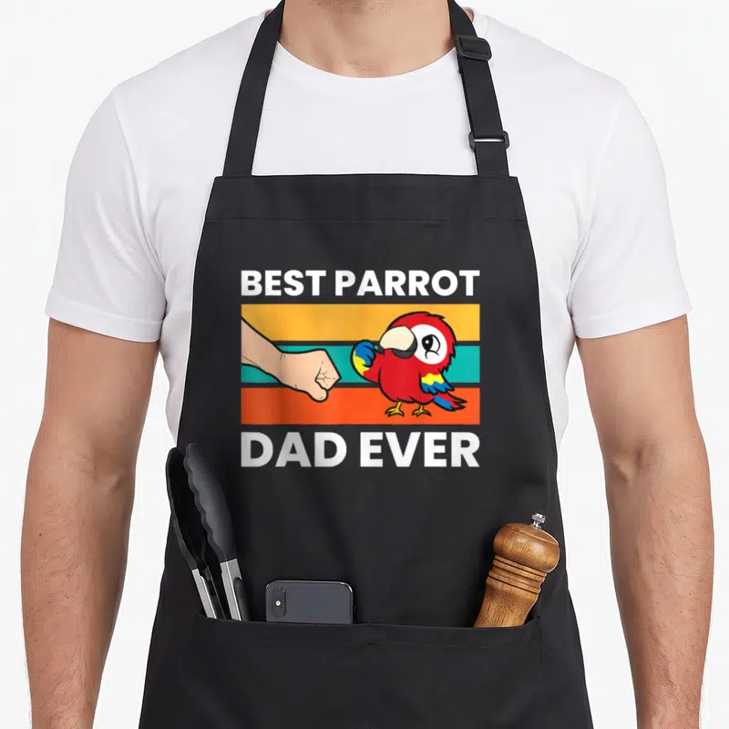 Scarlet papa apron - Cartoon red parrot fist-bumping human fist over orange teal and orange stripes with white text — shown on a black cotton canvas apron against a white background