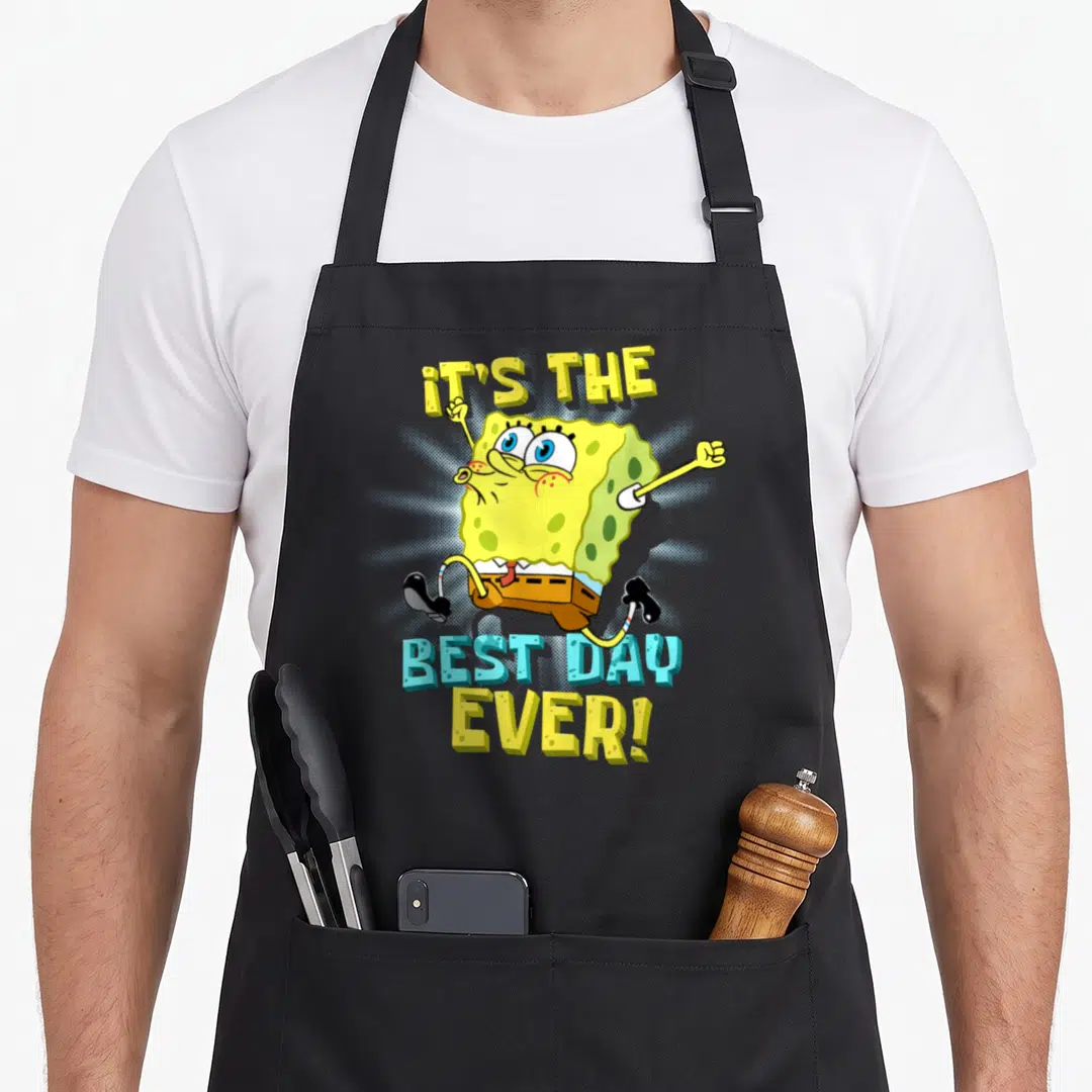 Cute age birthday apron for grilling - SpongeBob jumping between IT'S THE BEST DAY EVER text in yellow and blue — shown on a black cotton canvas apron against a white background
