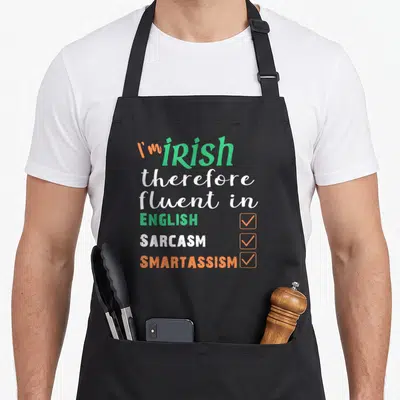 Irish smart apron - Stacked text I'm Irish fluent in English sarcasm smartassism with three checked boxes in green — shown on a black cotton canvas apron against a white background