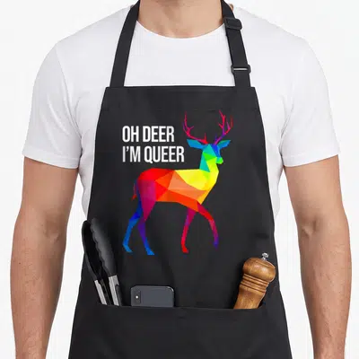 Deer gay pride apron - White text OH DEER I M QUEER beside geometric rainbow deer — shown on a black cotton canvas apron against a white background