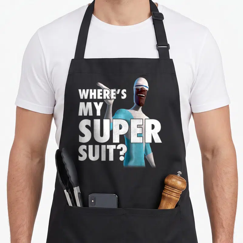 Frozone novelty apron - Stacked white text WHERE'S MY SUPER SUIT beside blue grey cartoon character pointing finger — shown on a black cotton canvas apron against a white background