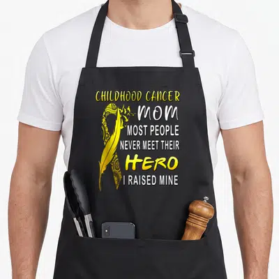 Childhood mom and son aprons - Yellow ribbon feather with text CHILDHOOD CANCER MOM HERO I RAISED MINE — shown on a black cotton canvas apron against a white background