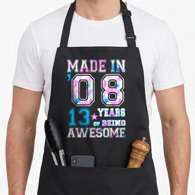 13th born day apron - Stacked tie-dye text Made in 08 13 Years of Being Awesome with pink star — shown on a black cotton canvas apron against a white background